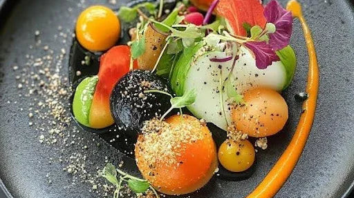 Gourmet dish with colorful vegetable spheres, microgreens, edible flowers, and vibrant sauces on a black plate