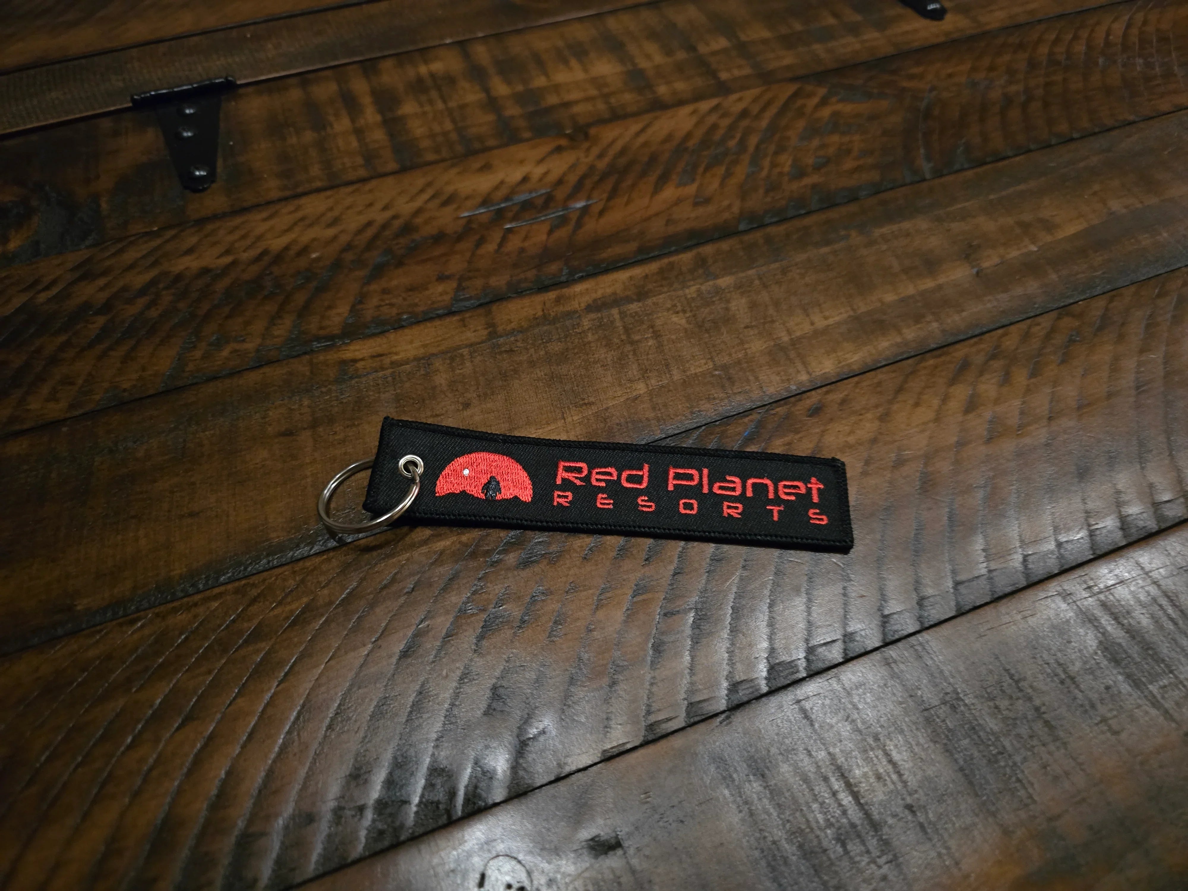 Red Planet Resorts keychain on rustic wooden surface with black fabric and red text