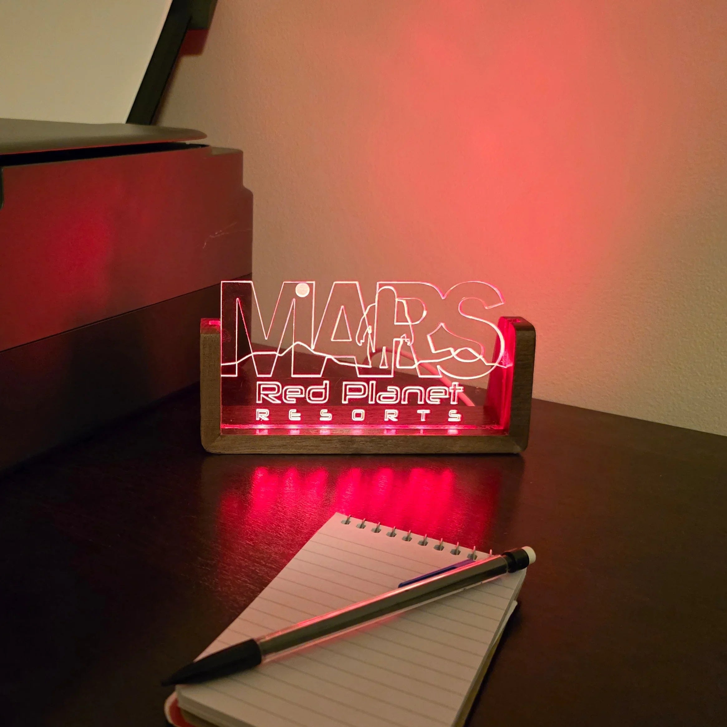 Red LED light decoration with Mars Red Planet Resorts text on a desk next to notepad and pen