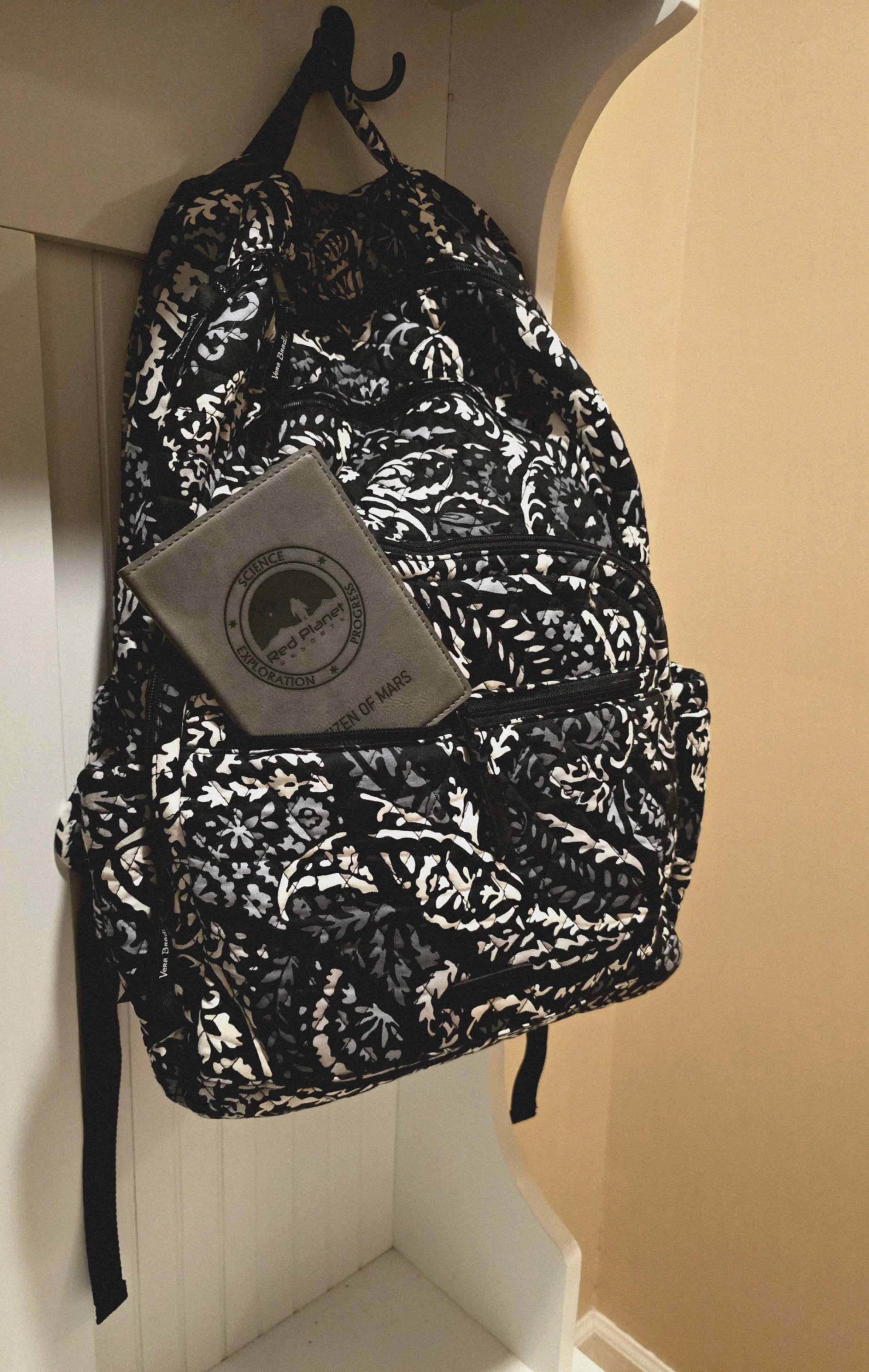 Black and white patterned backpack hanging on hook with a gray notebook labeled Red Planet Science Exploration