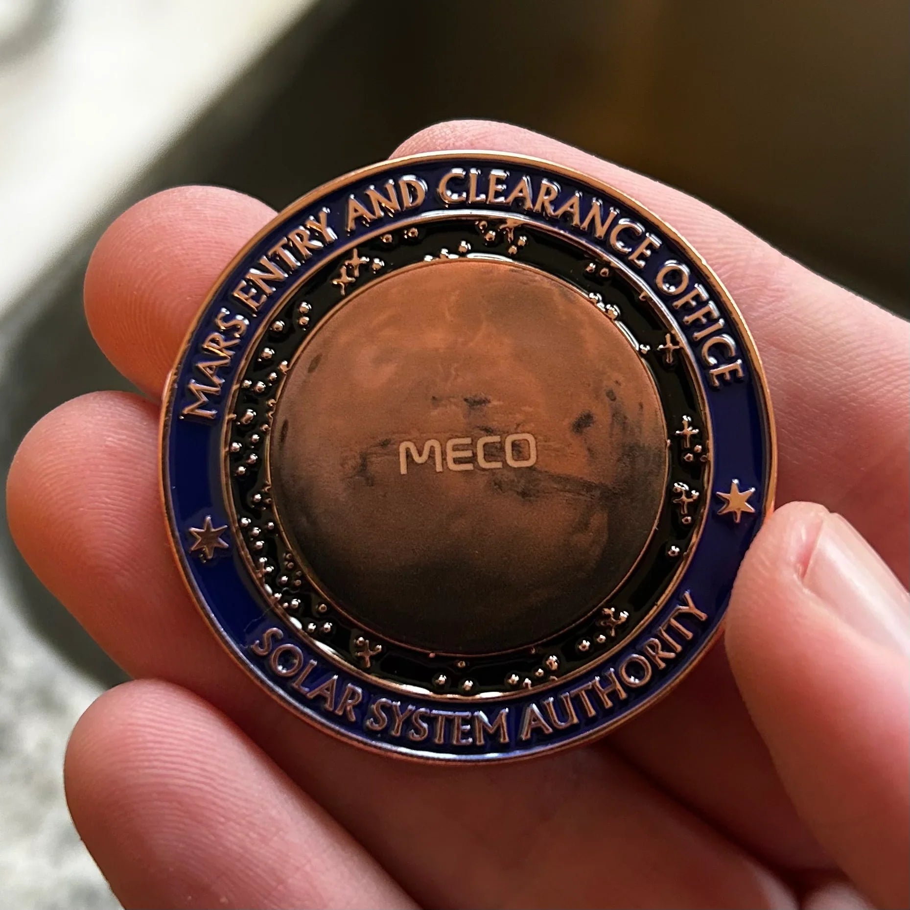 Close-up of a Mars Entry and Clearance Office coin held by fingers, featuring Mars planet design and Solar System Authority text