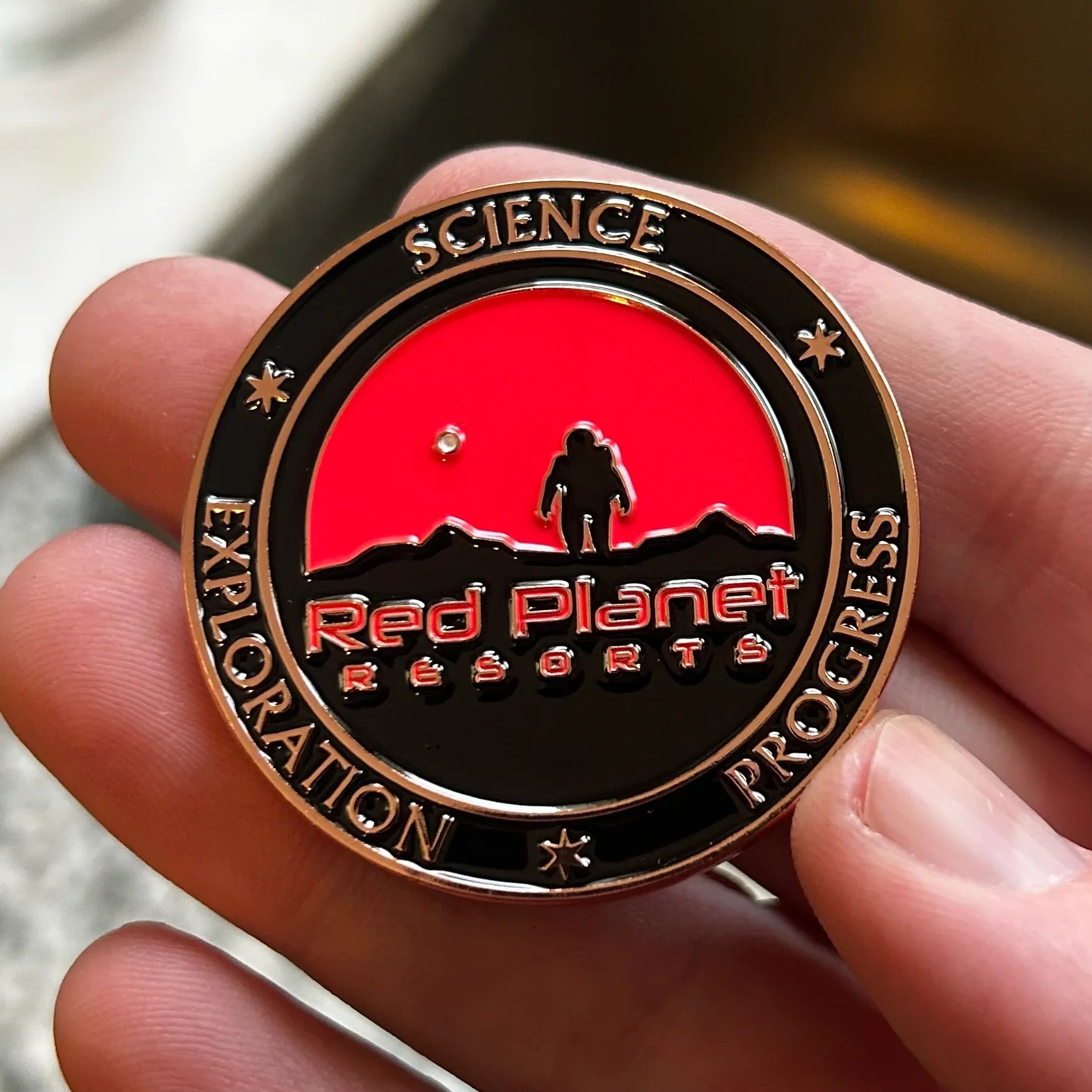 Hand holding Red Planet Resorts coin with astronaut and Mars landscape design