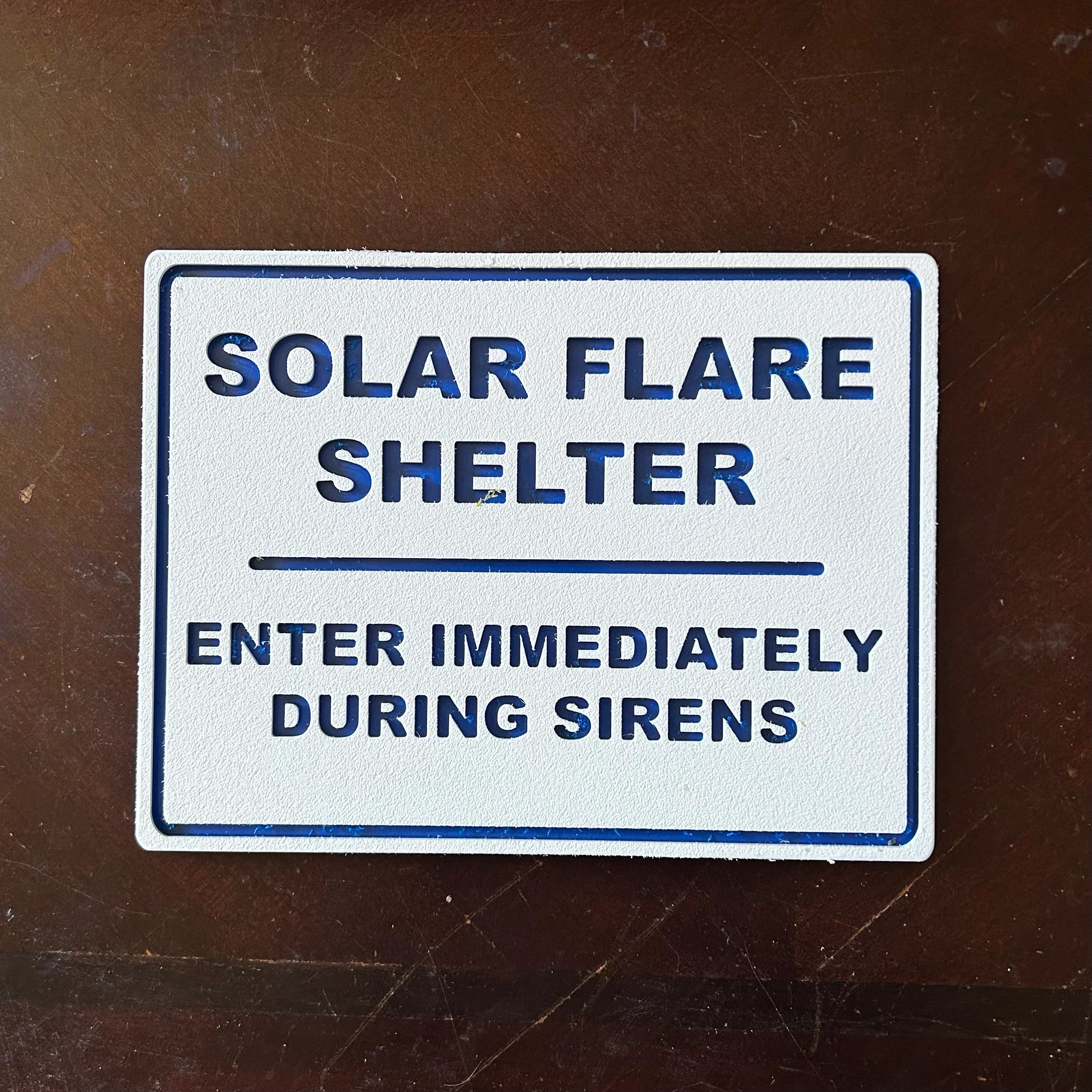 White metal sign on dark surface with text Solar Flare Shelter enter immediately during sirens