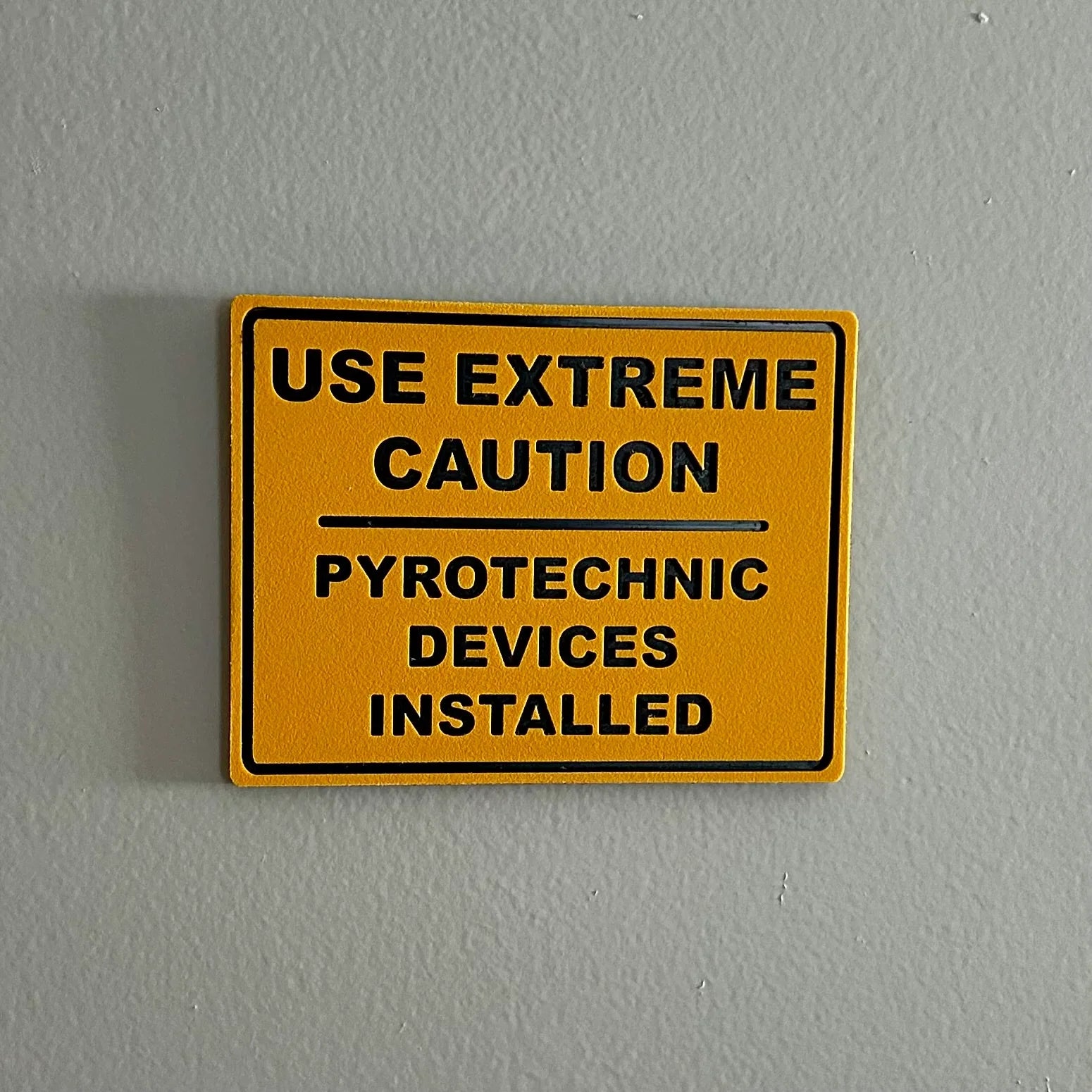 Yellow caution sign on gray wall reading Use Extreme Caution Pyrotechnic Devices Installed