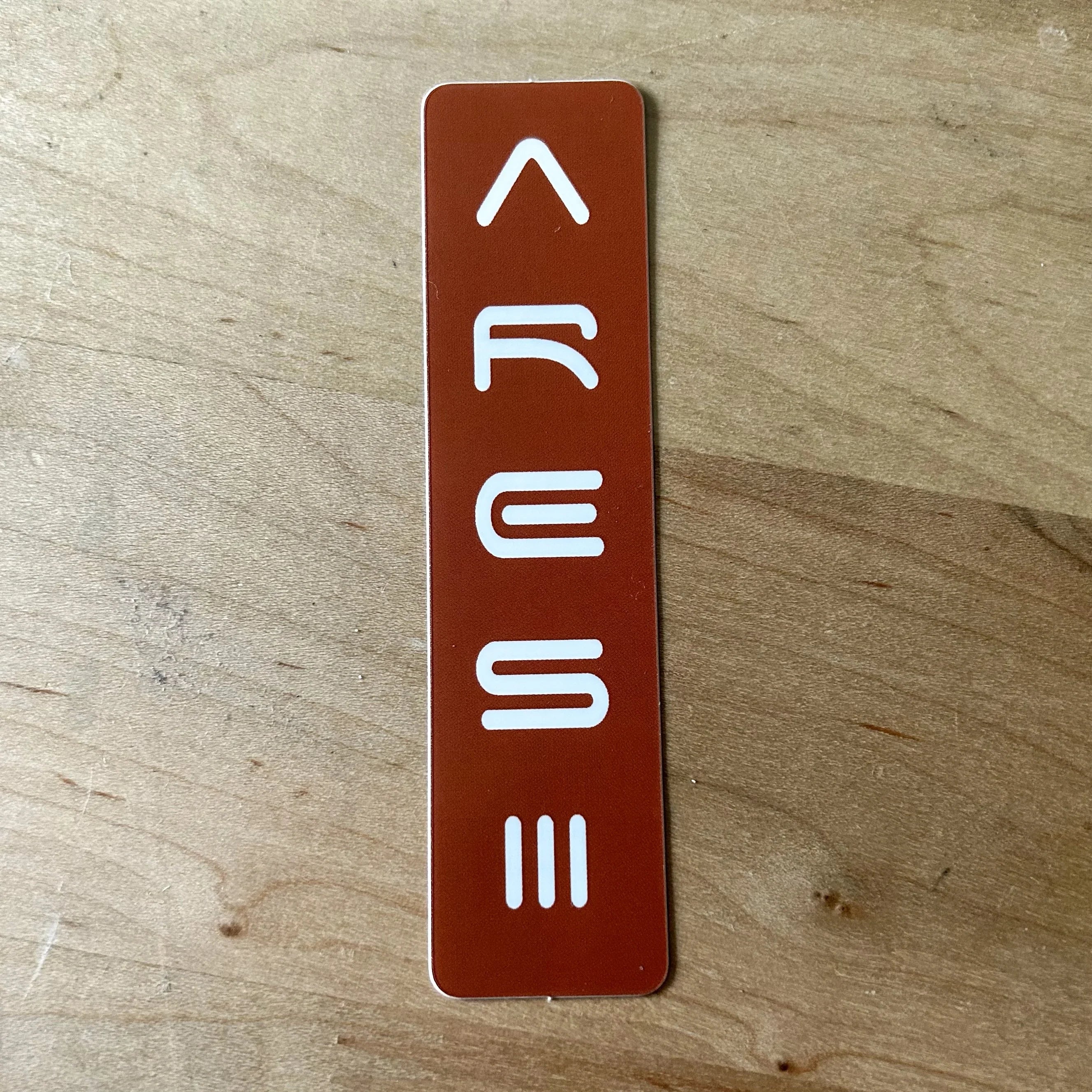 Close-up of a red vertical sticker with white stylized letters spelling ARIES on a wooden surface