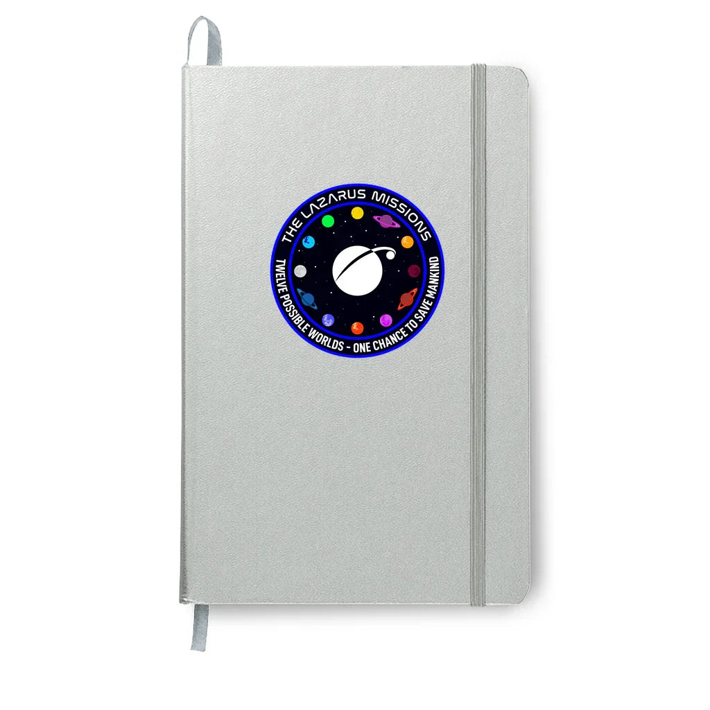 Gray notebook with elastic band featuring The Lazarus Missions space patch with planets and stars