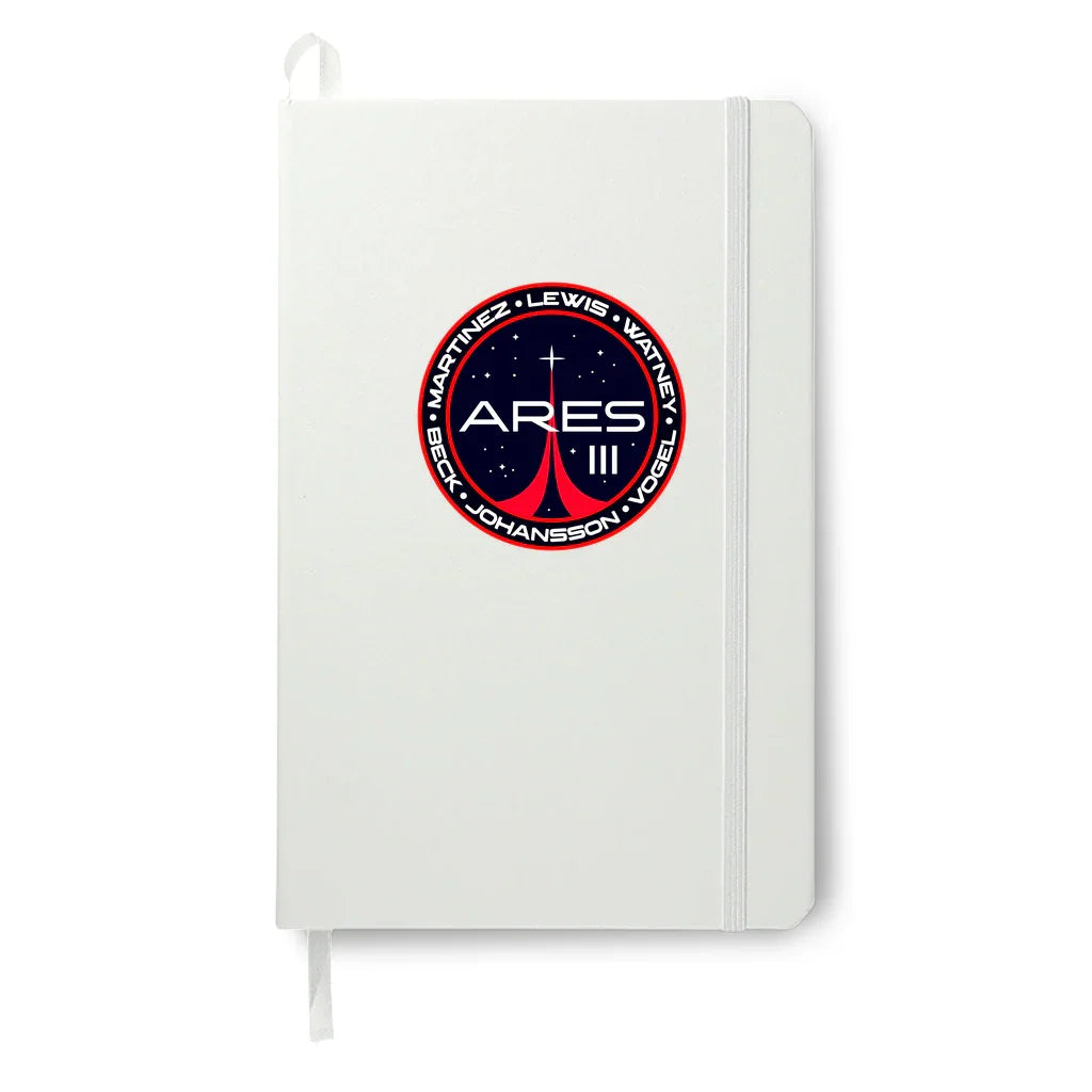 White notebook with elastic band and Ares III space mission patch featuring astronaut names and stars