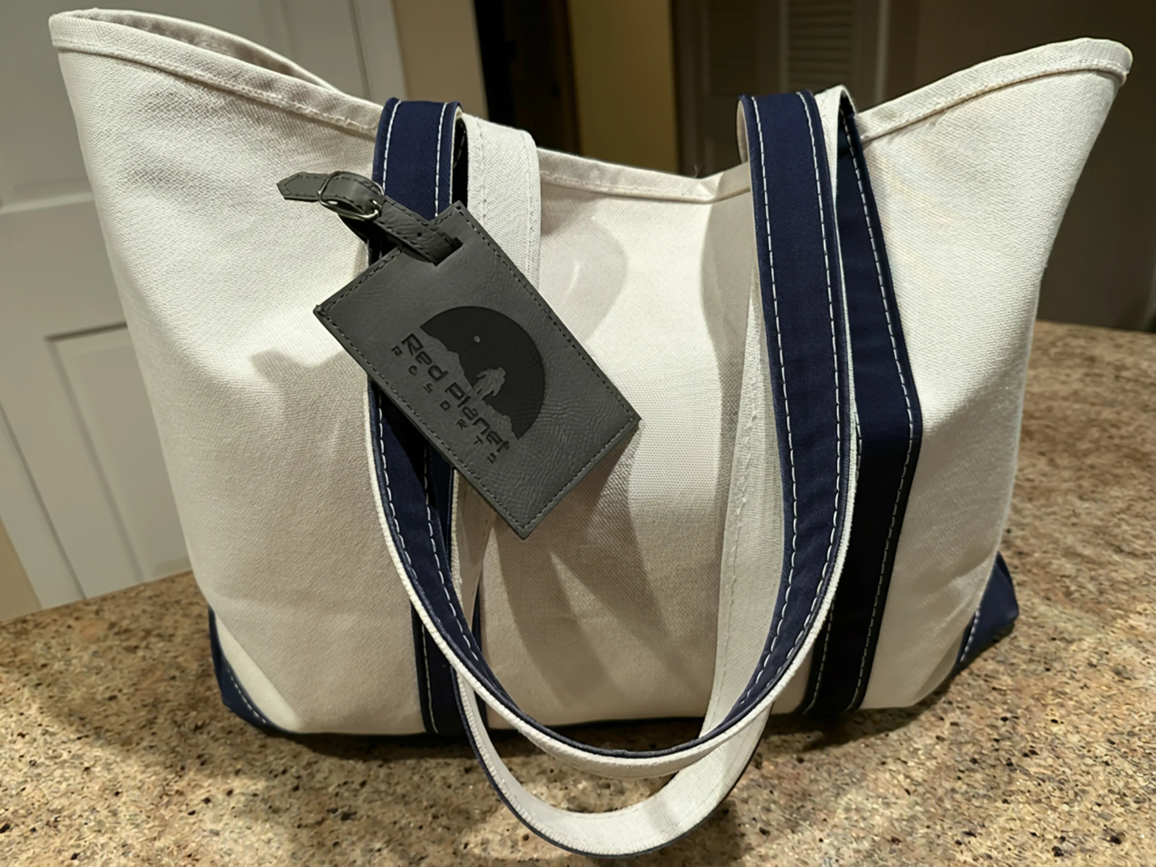 Beige canvas tote bag with navy blue straps and a Red Planet Resorts luggage tag on a countertop