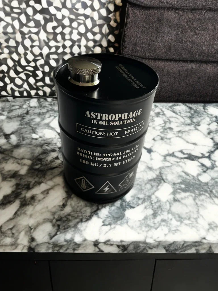 Black metal container labeled Astrophage in oil solution, placed on marble countertop with patterned and fabric background