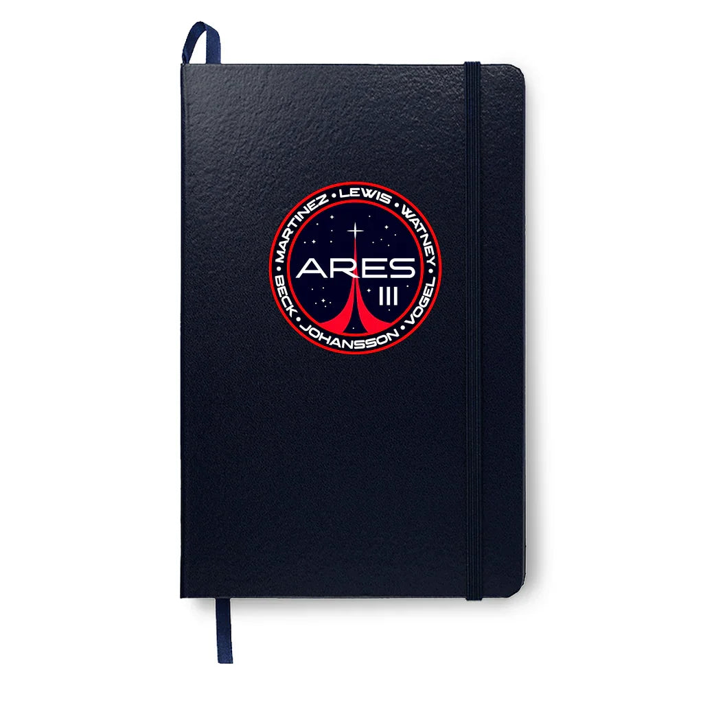 Black notebook with elastic band and Ares III space mission patch featuring astronaut names and star graphics