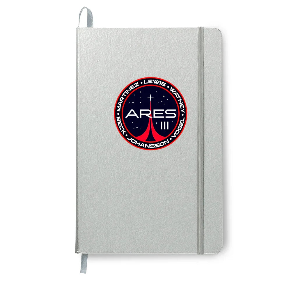 Silver notebook with elastic band featuring Ares III space mission logo with names Martinez, Lewis, Watney, Beck, Johansson, Vogel