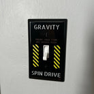 Light switch with 'Gravity' and 'Spin Drive' labels on a gray wall.