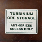 Beige sign with green text reading Turbinum Ore Storage Authorized Access Only on brown surface