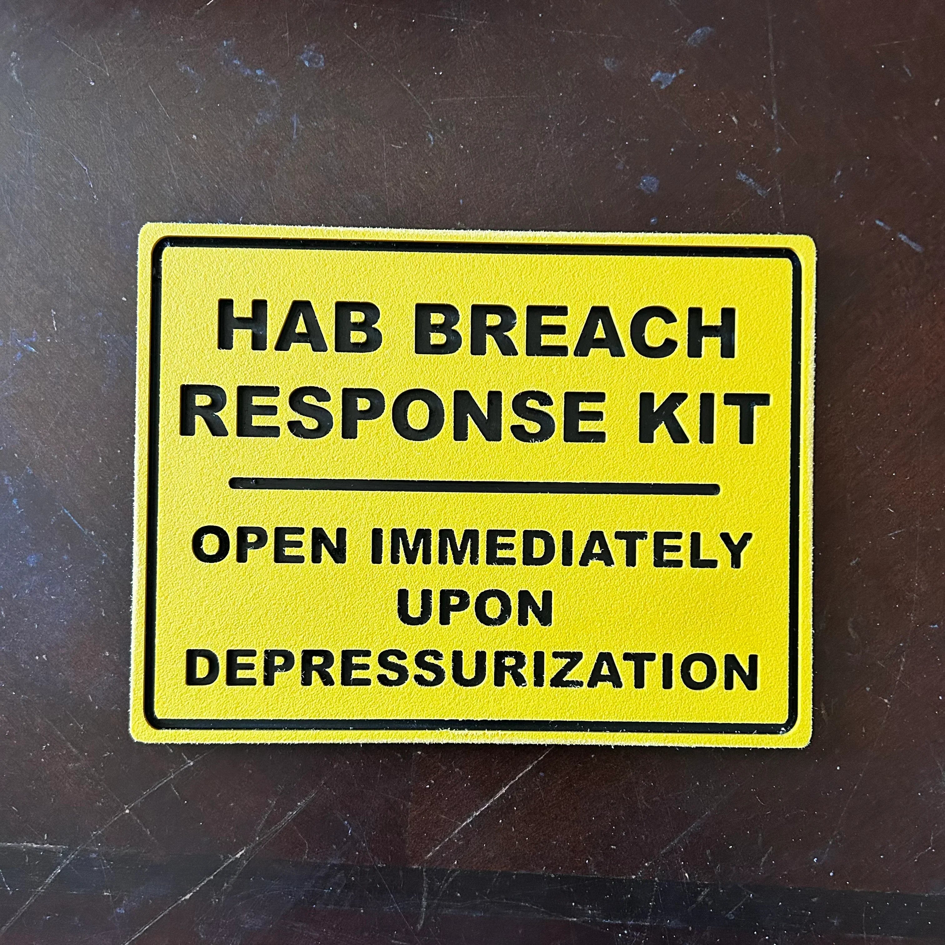 Yellow sign for HAB Breach Response Kit with instructions to open immediately upon depressurization