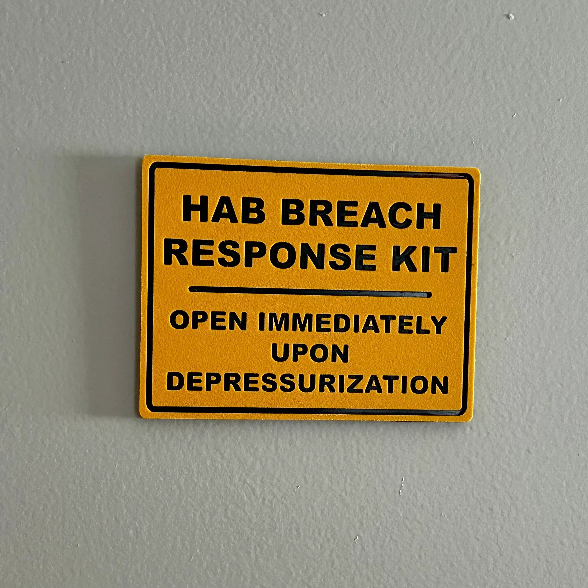 Yellow warning sign reading HAB breach response kit open immediately upon depressurization