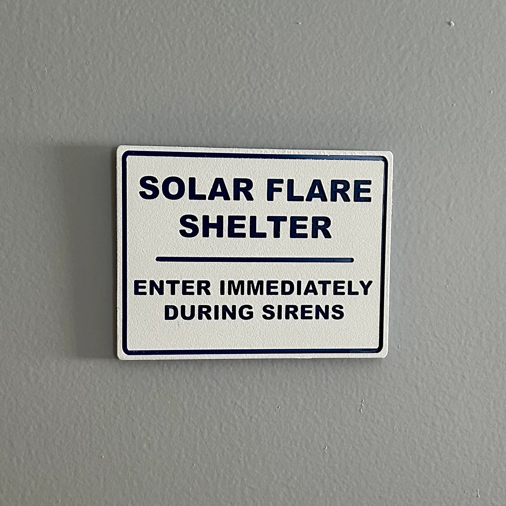 White sign on gray wall reading Solar Flare Shelter, enter immediately during sirens