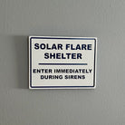White sign on gray wall reading Solar Flare Shelter, enter immediately during sirens