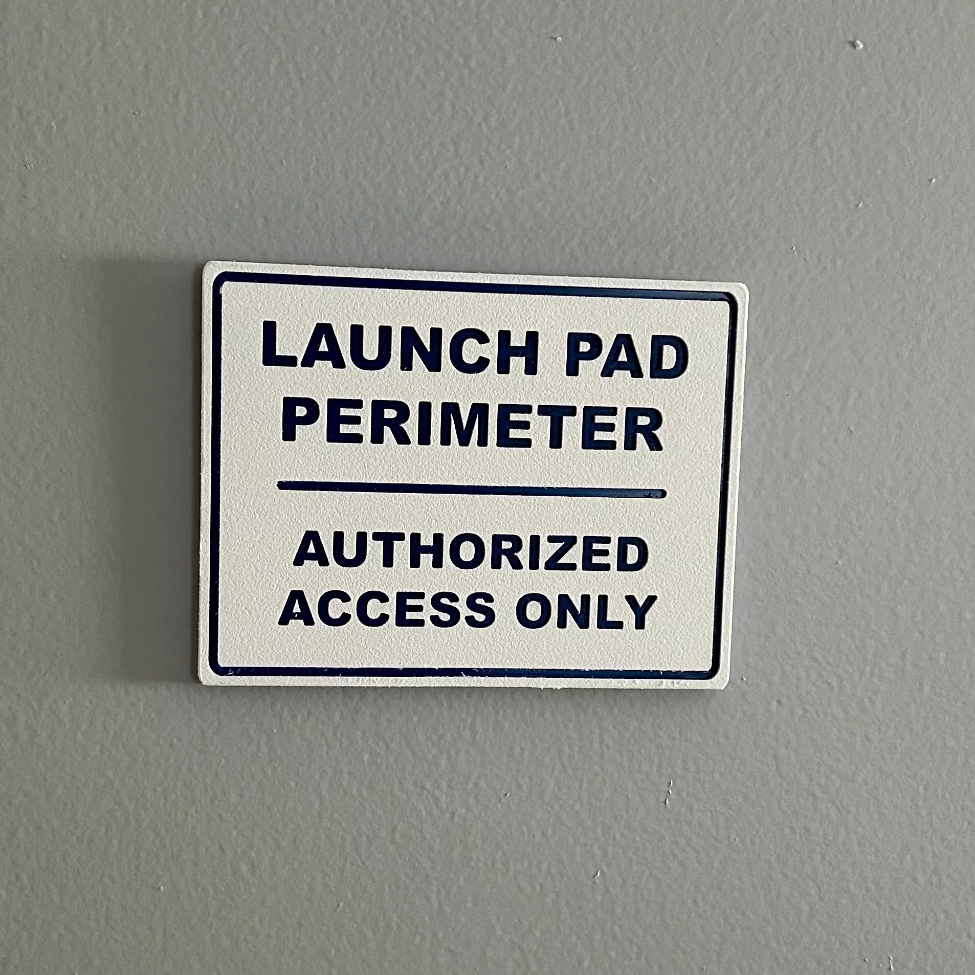 White sign with black text on gray wall reading Launch Pad Perimeter Authorized Access Only