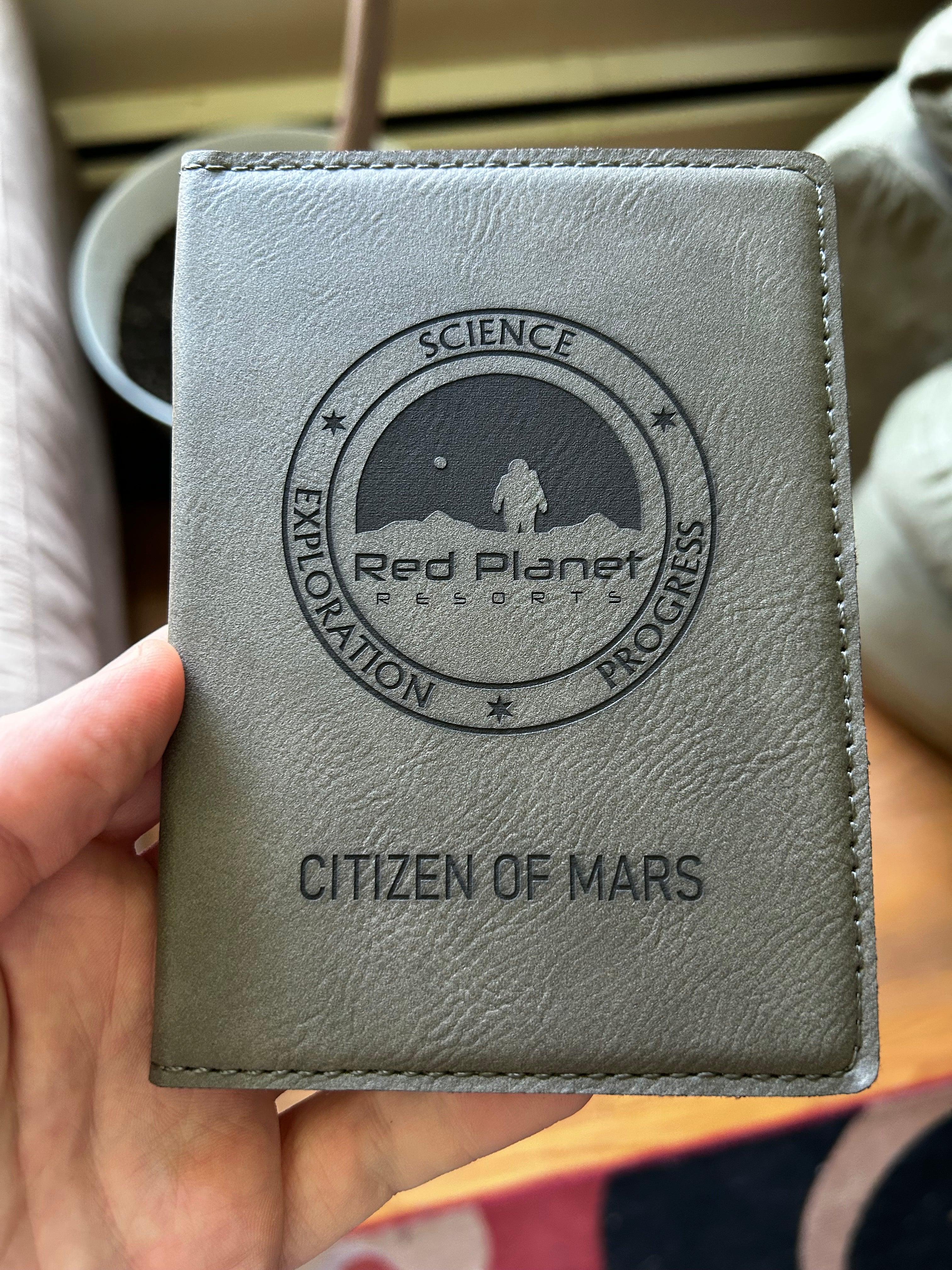 Gray leather passport cover with Red Planet Resorts logo and Citizen of Mars text held by hand
