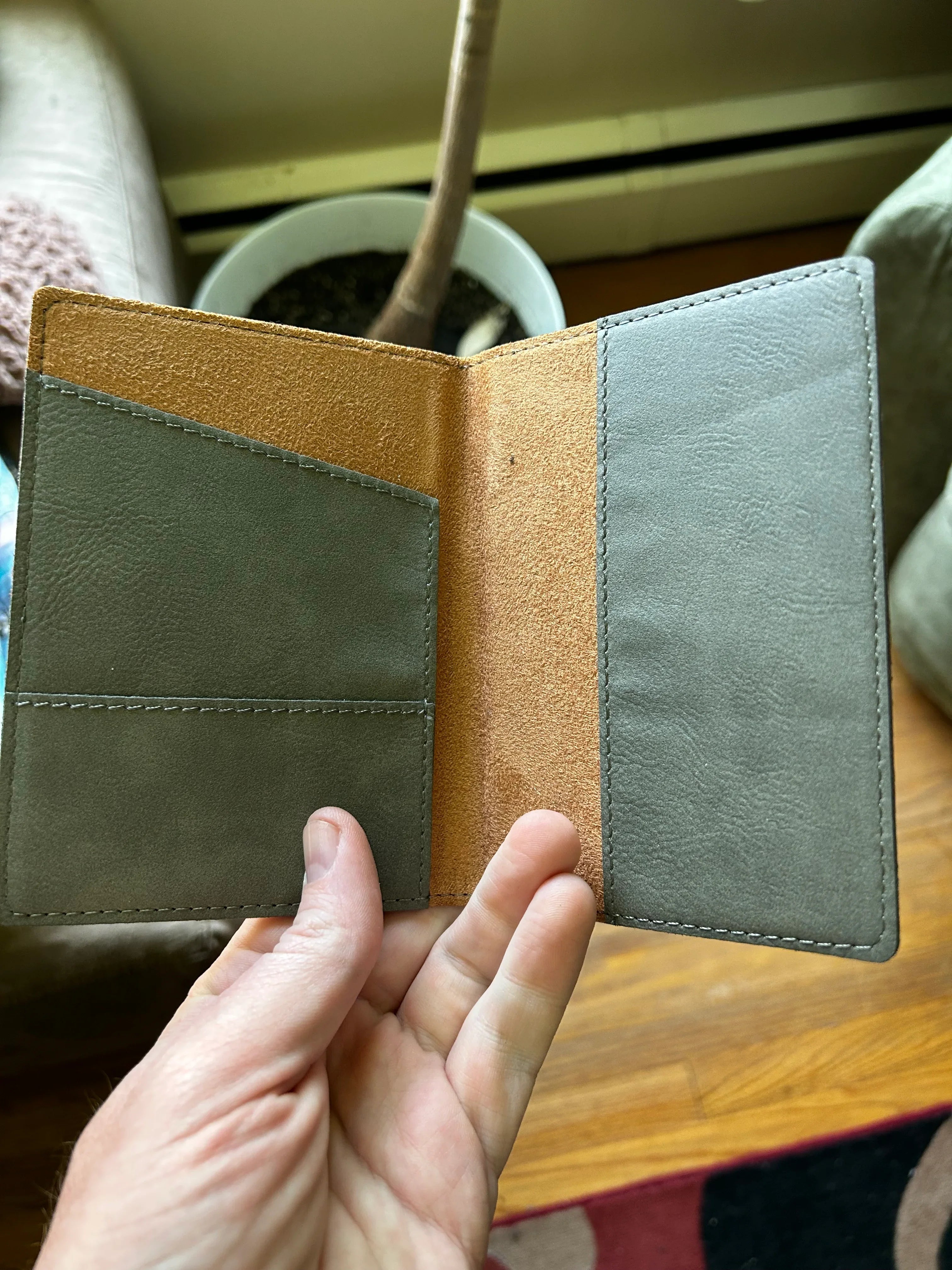 Hand holding open gray and tan leather wallet with multiple card slots indoor setting