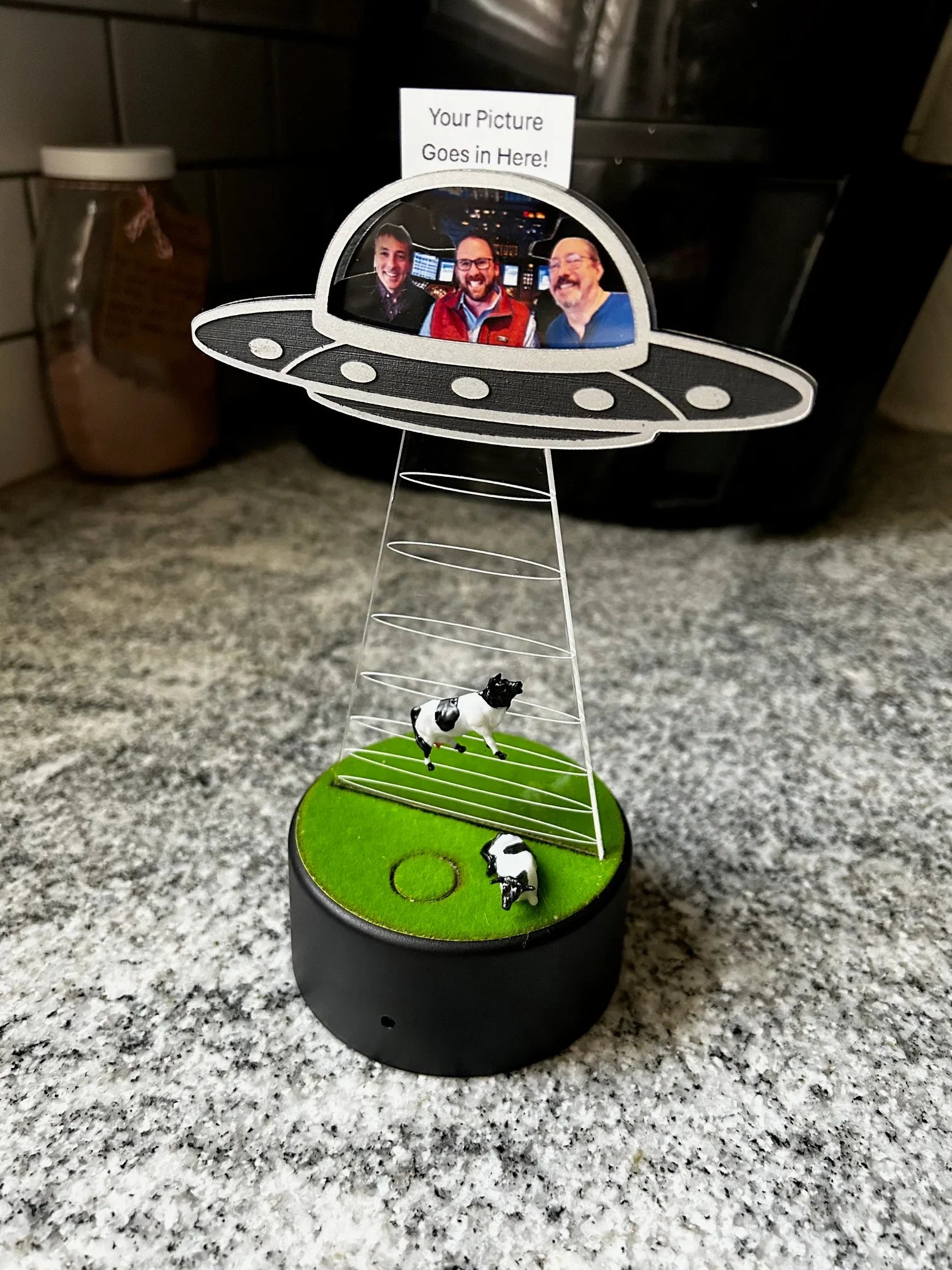 Miniature UFO model with three men photo, two cows on green base, on kitchen counter