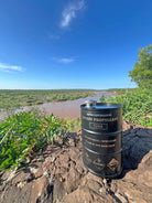Black metal barrel labeled methyhhydrazine rocket propellant on rocky riverbank under clear blue sky