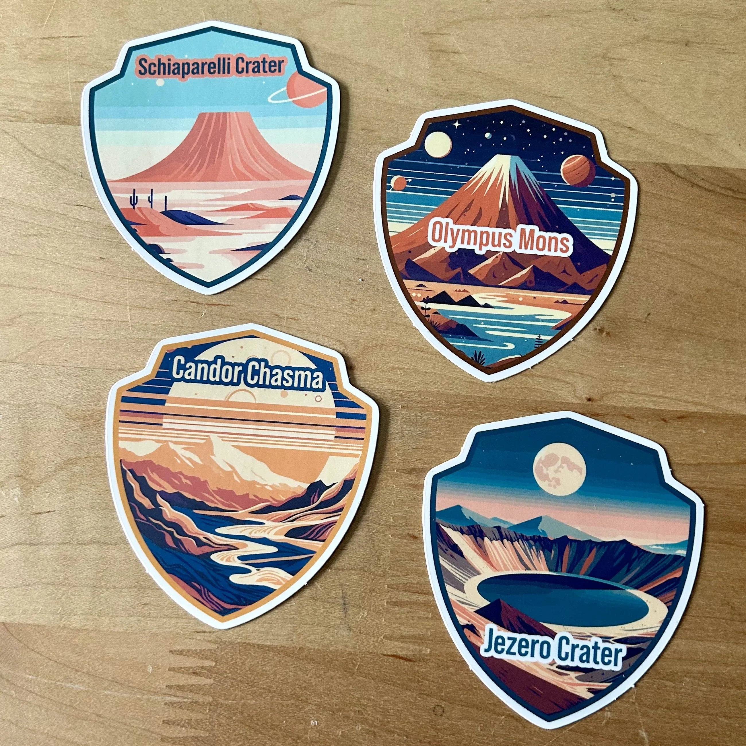 Four space-themed shield stickers depicting Martian landmarks Schiaparelli Crater, Olympus Mons, Candor Chasma, and Jezero Crater