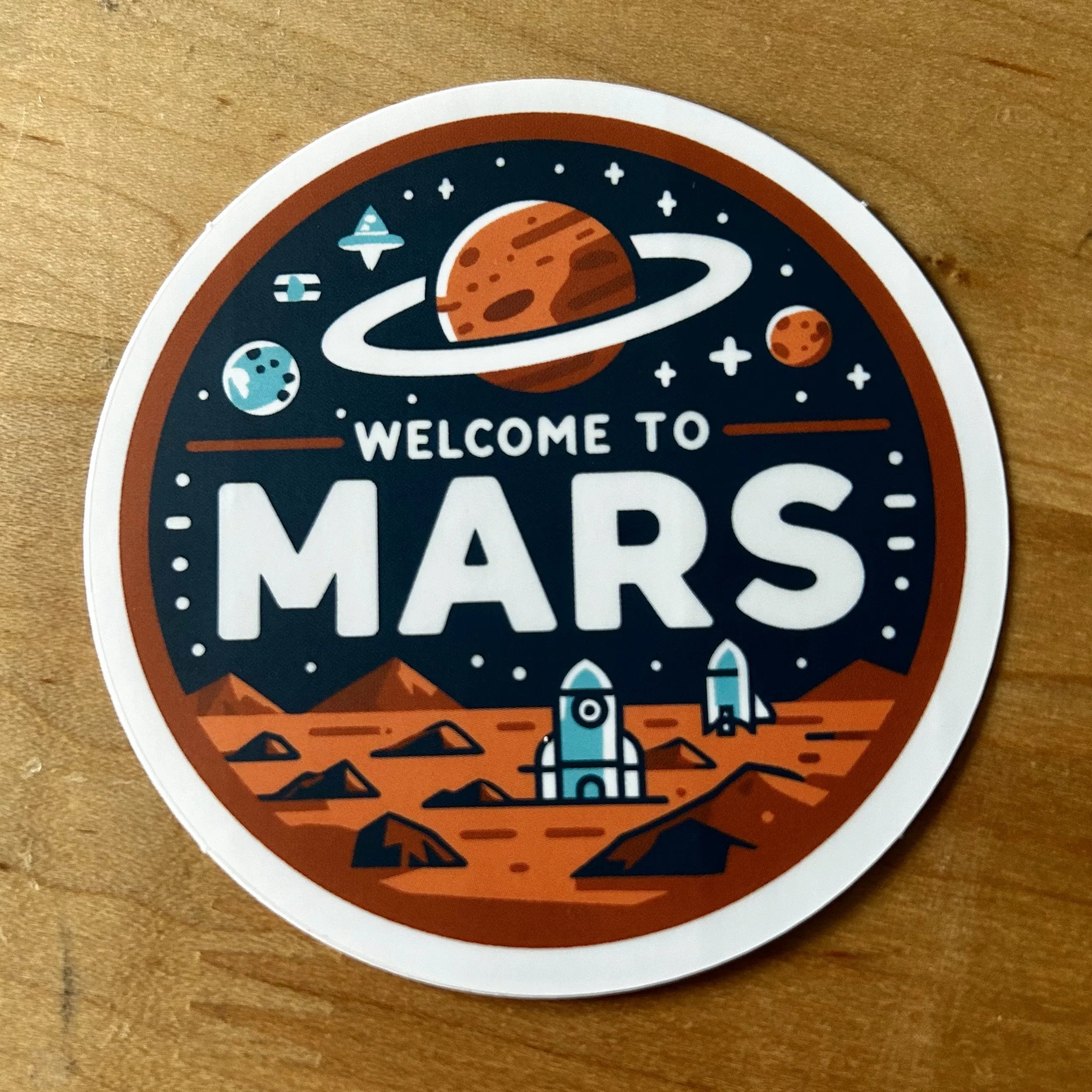 Round sticker showing Mars landscape with rockets and planets, text Welcome to Mars