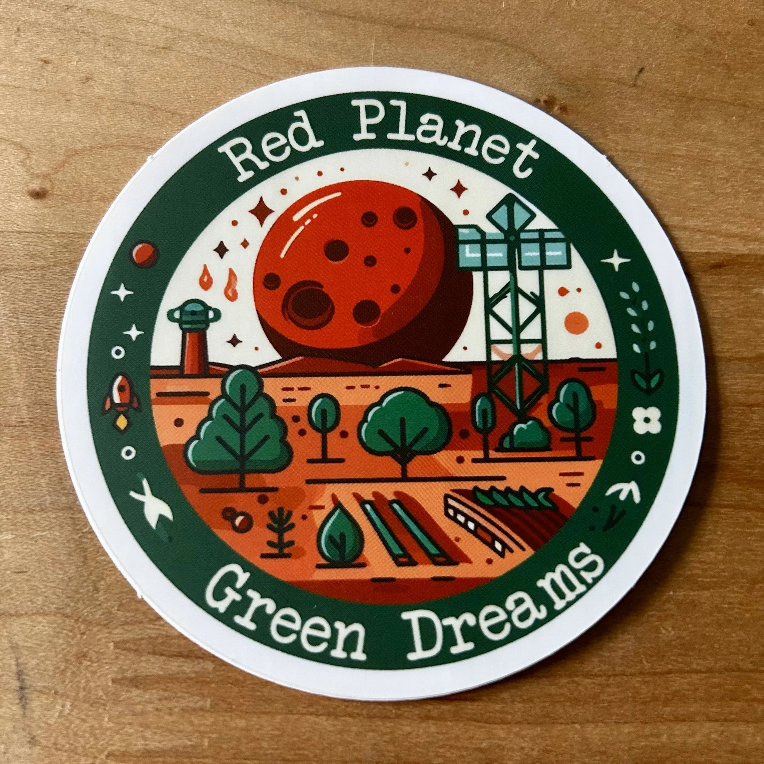 Circular sticker with illustration of red planet, green trees, telescope, and text 'Red Planet Green Dreams'