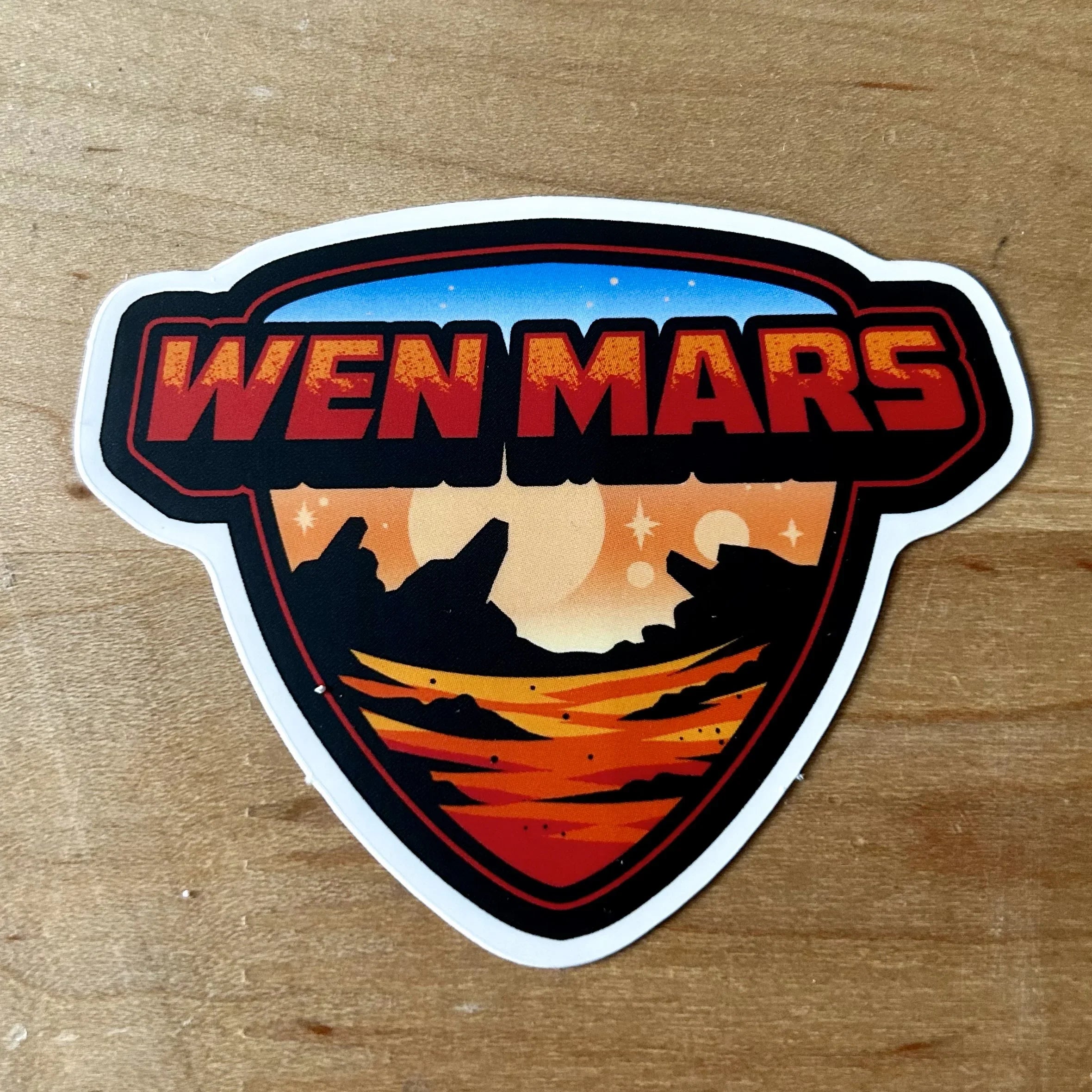 Wen Mars sticker with red text and Mars landscape design on wooden surface
