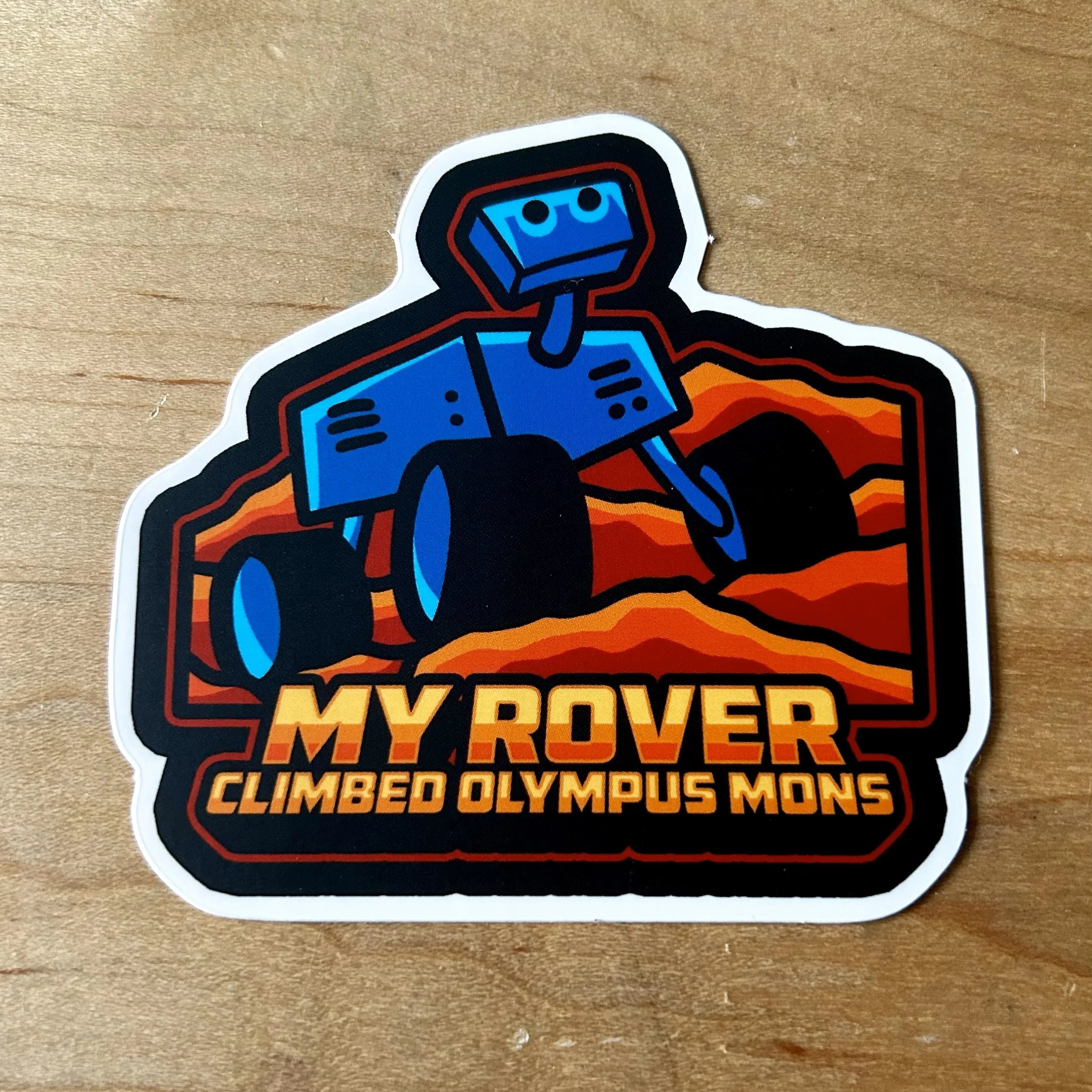 Sticker of blue Mars rover on red rocky terrain with text My Rover Climbed Olympus Mons