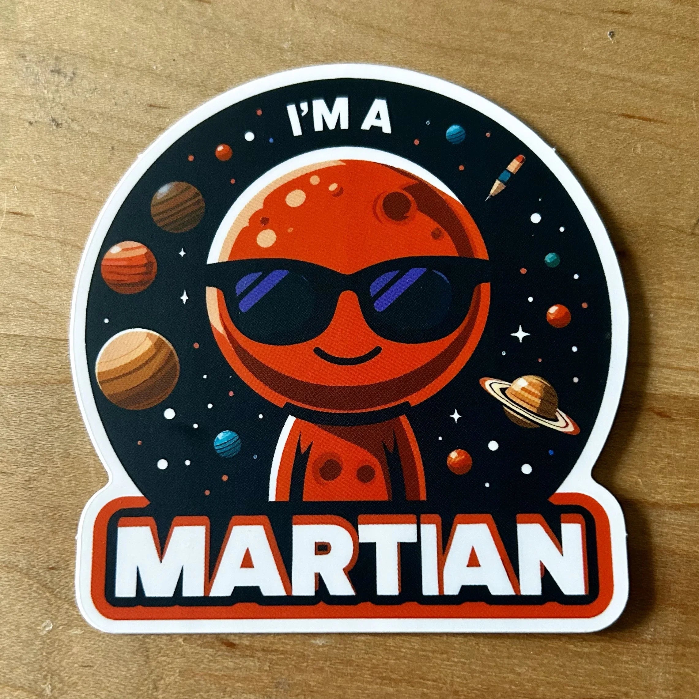 Sticker of a smiling red Martian with sunglasses, planets, stars, and text saying I'm a Martian