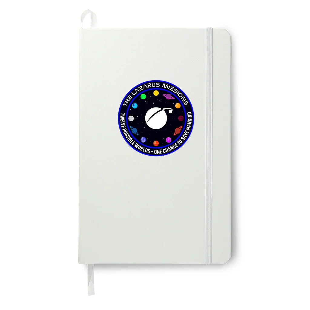 White notebook with The Lazarus Missions space-themed patch featuring colorful planets and mission slogan.