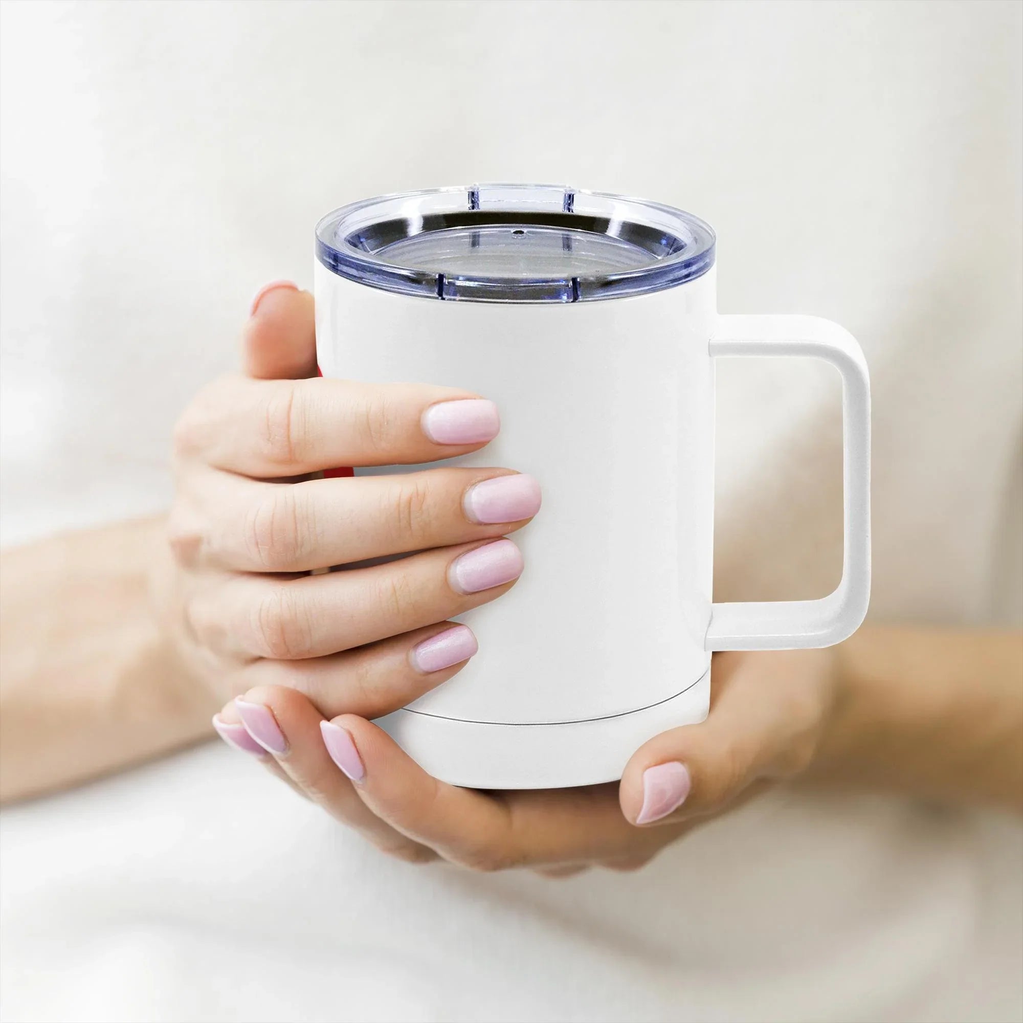 Close-up of hands holding a white insulated travel mug with a clear plastic lid